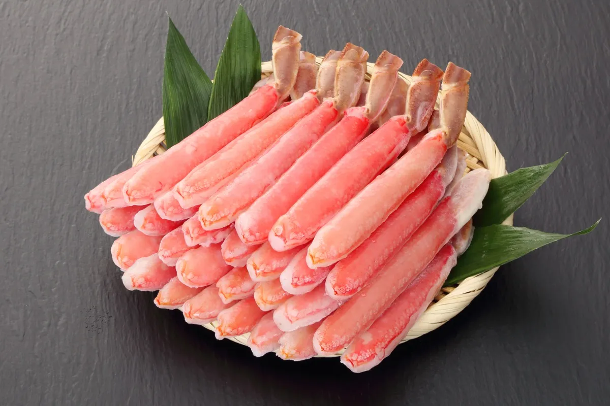 生ずわいの脚肉のむき身が、笹の葉を敷いたざるに山のように盛られている写真